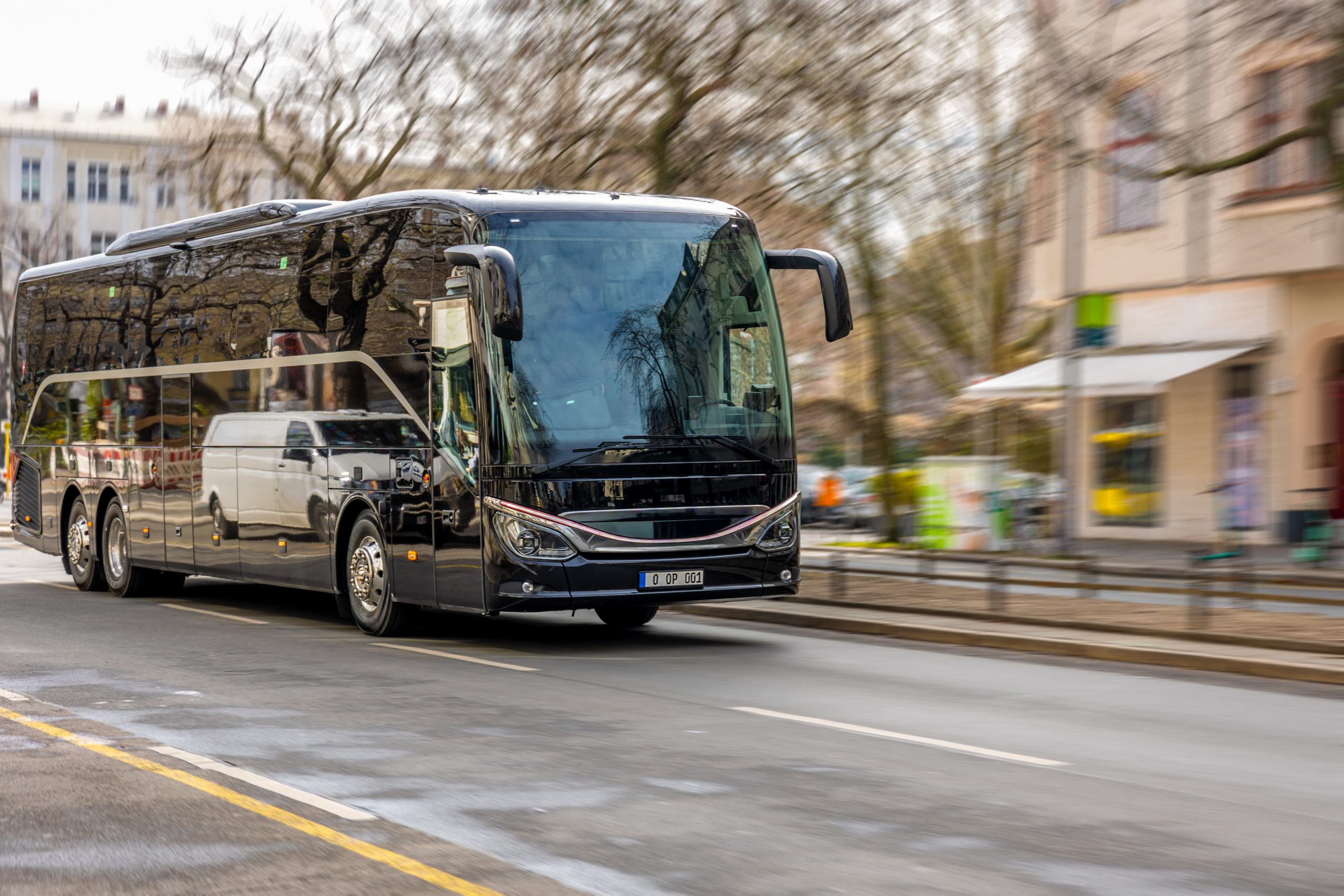 Black tourist bus driving on the road. Modern passenger coach moving through city.